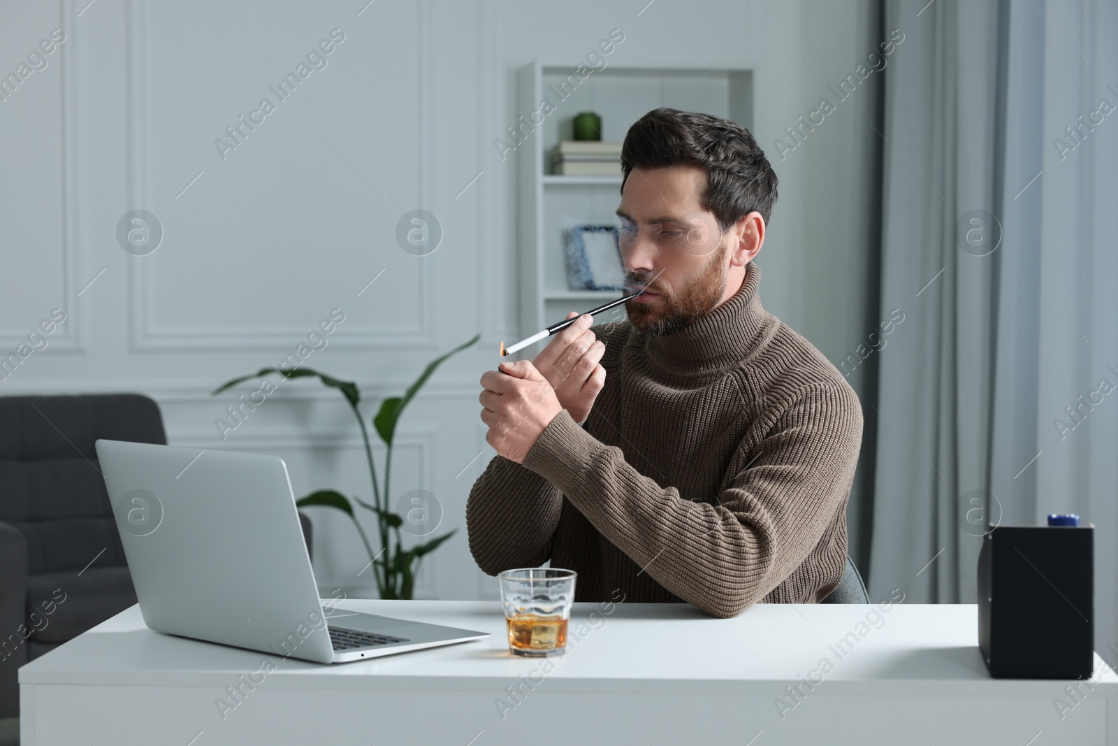 Photo of Man using long cigarette holder for smoking at workplace in office