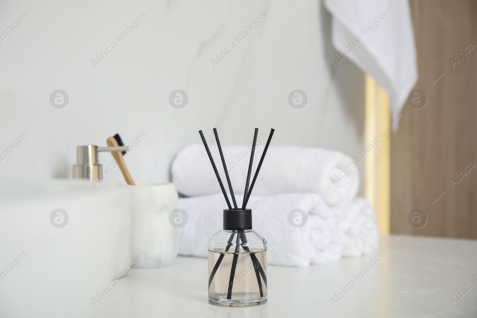 Photo of Aromatic reed air freshener, toiletries and towels on white countertop in bathroom