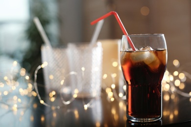 Photo of Glass of cold cola and fairy lights on table. Space for text