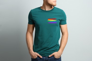 Image of Young man wearing green t-shirt with image of LGBT pride flag on light grey background