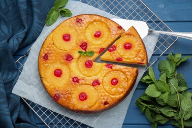 Delicious cut pineapple pie with cherry and mint on blue wooden table, flat lay