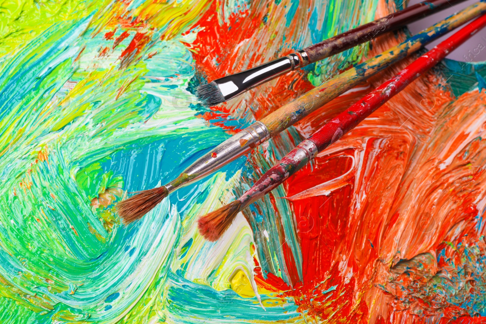 Photo of Closeup view of artist's palette with mixed paints and brushes as background