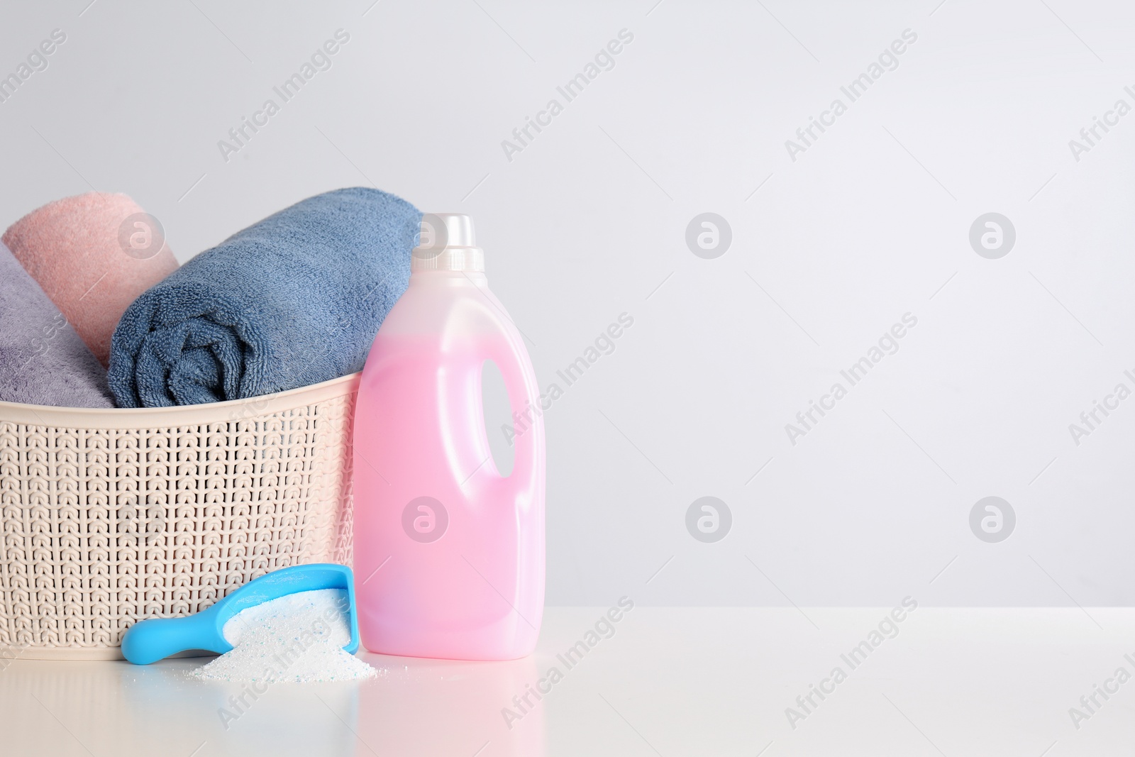 Photo of Detergents and basket with clean towels on white background, space for text. Laundry day