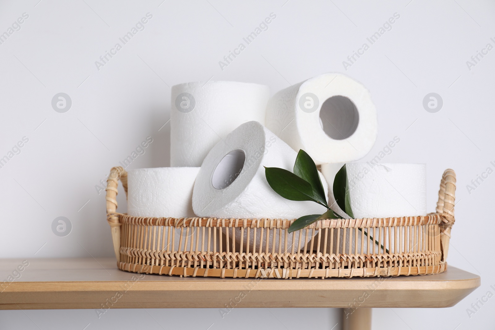 Photo of Toilet paper rolls and green leaves on wooden table near white wall