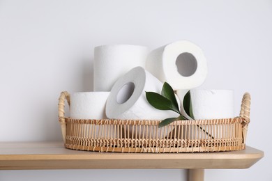Toilet paper rolls and green leaves on wooden table near white wall