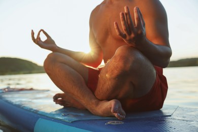Man meditating on light blue SUP board on river at sunset, closeup