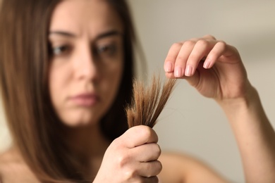 Photo of Woman with damaged hair on blurred background, selective focus. Split ends