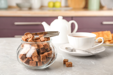Photo of Glass bowl with brown sugar cubes and tongs on grey table