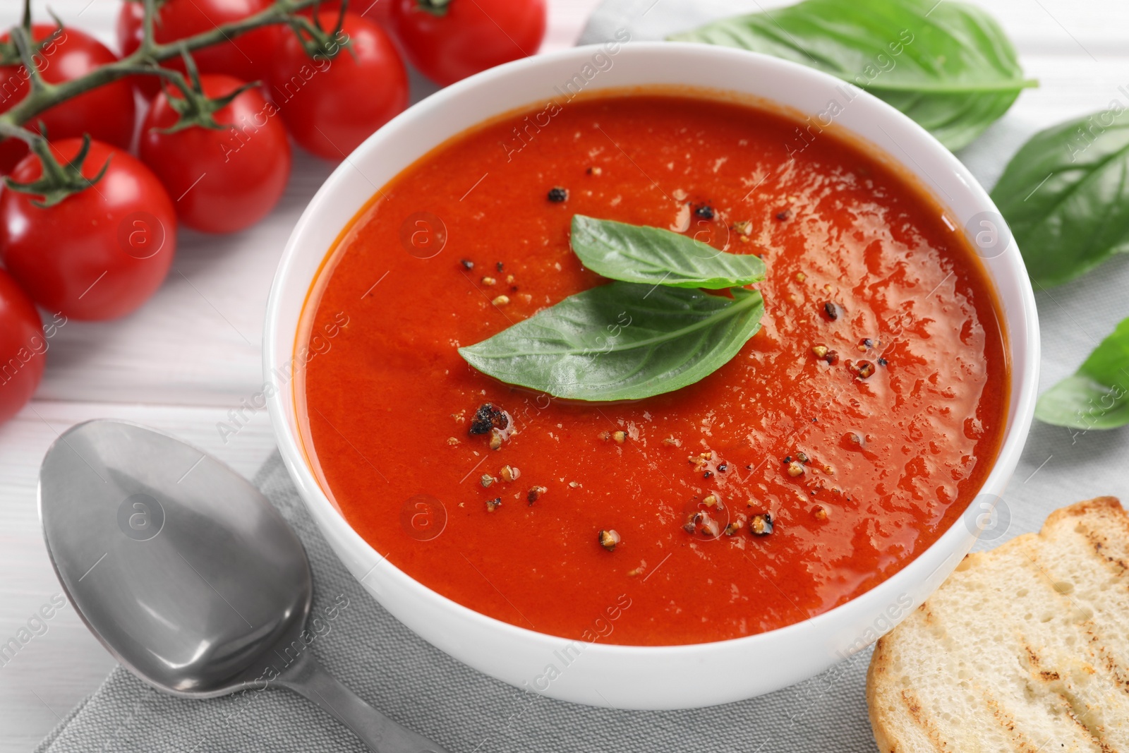 Photo of Delicious tomato cream soup in bowl served on white wooden table, closeup