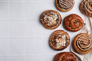 Sweet buns. Delicious rolls with raisins and toppings on white tiled table, flat lay. Space for text