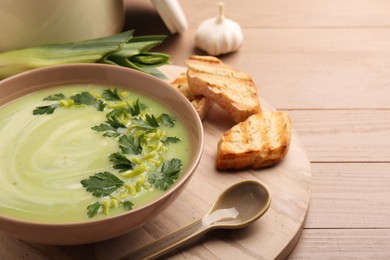 Photo of Delicious leek soup served on beige wooden table, closeup. Space for text