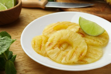 Photo of Tasty grilled pineapple slices and piece of lime on wooden table, closeup