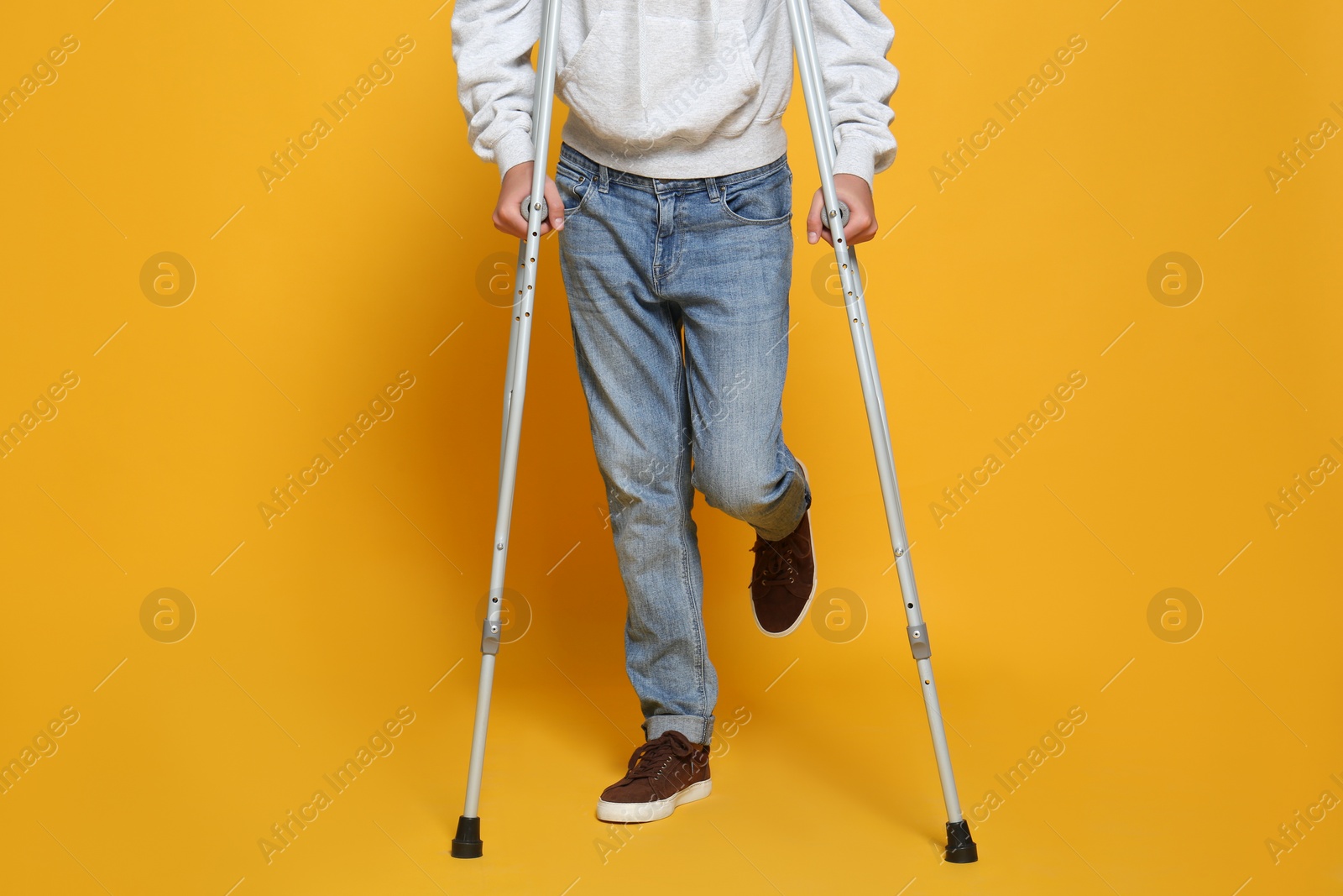 Photo of Man with injured leg using crutches on yellow background, closeup