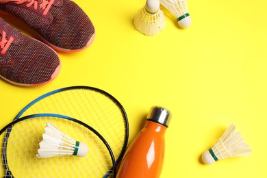 Photo of Feather badminton shuttlecocks, rackets, sneakers and bottle on yellow background, above view. Space for text