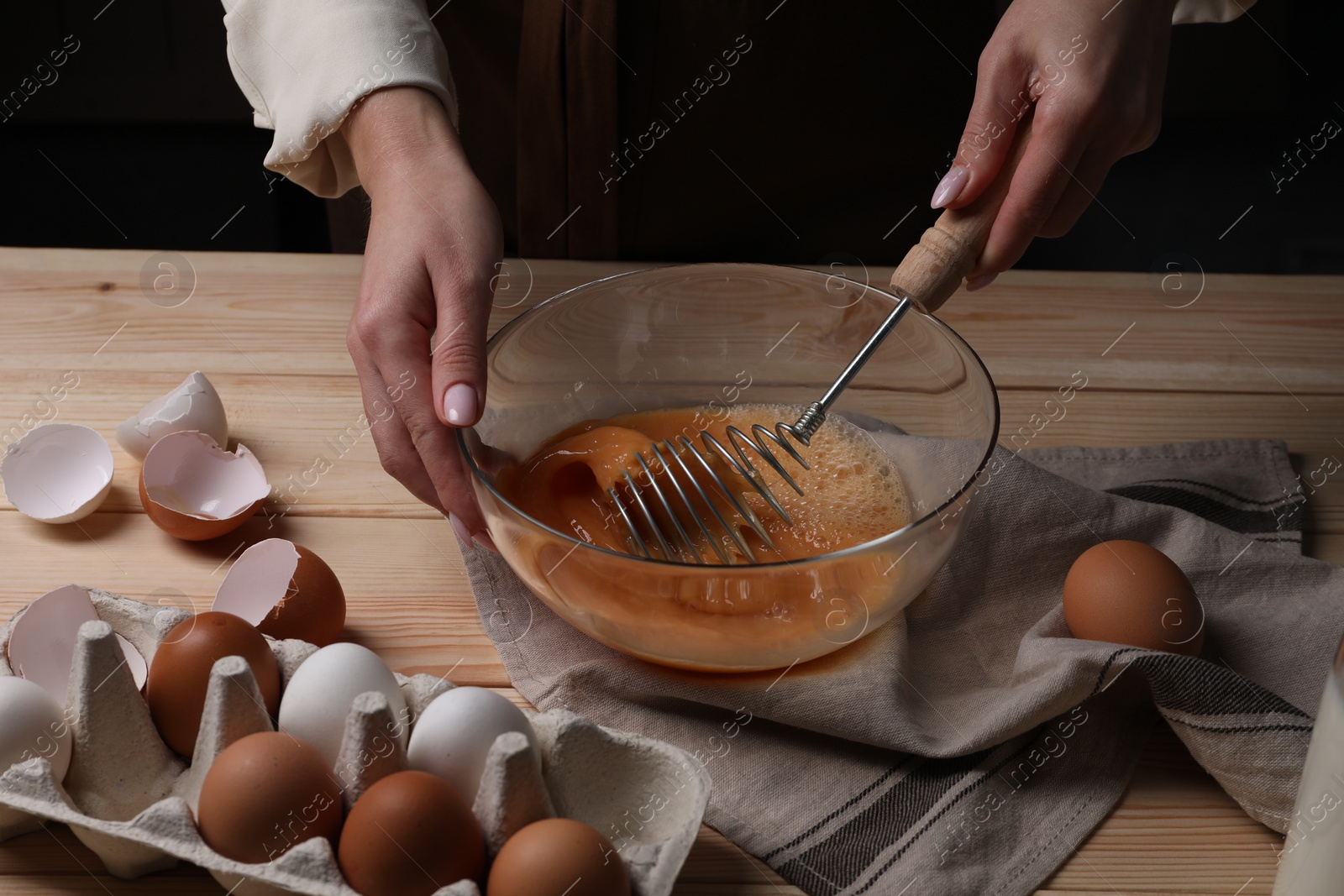 Photo of Woman whisking eggs in bowl at table, closeup