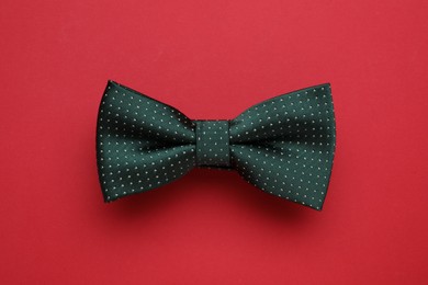 Photo of Stylish black bow tie with polka dot pattern on red background, top view