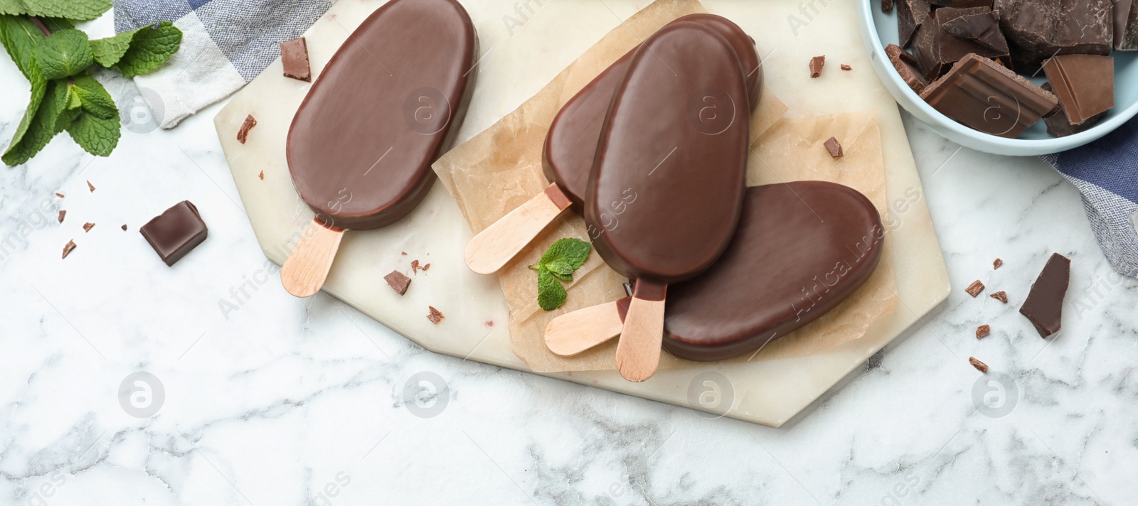Image of Delicious glazed ice cream bars with mint and chocolate on white marble table, flat lay. Banner design