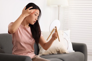Photo of Suffering from allergy. Young woman with mirror checking her face in living room