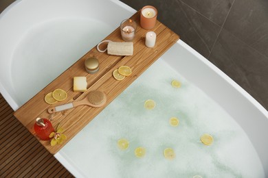 Photo of Wooden bath tray with candles and bathroom amenities on tub indoors, above view