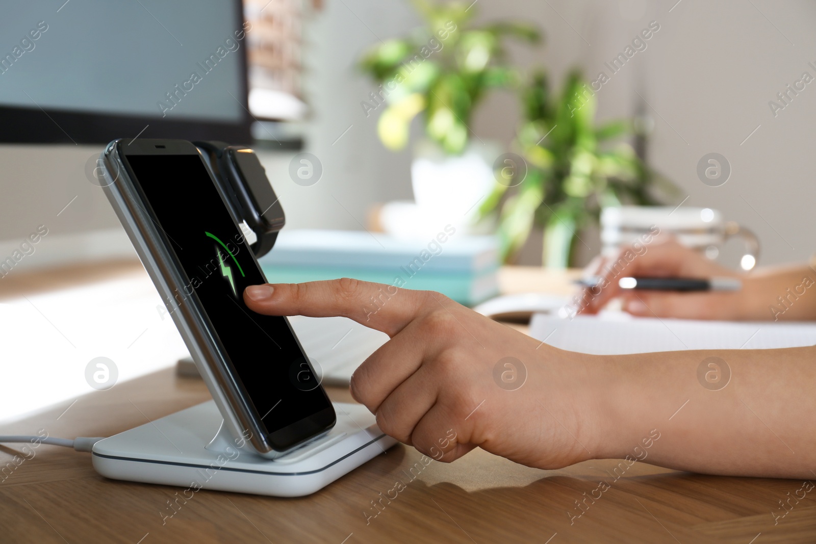 Photo of Woman at desk, smartphone and watch on wireless charger, closeup. Modern workplace