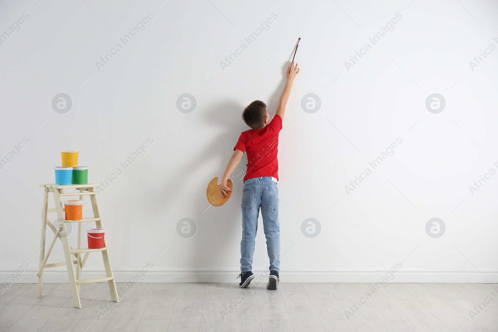 Photo of Little child painting on blank white wall indoors