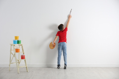 Photo of Little child painting on blank white wall indoors