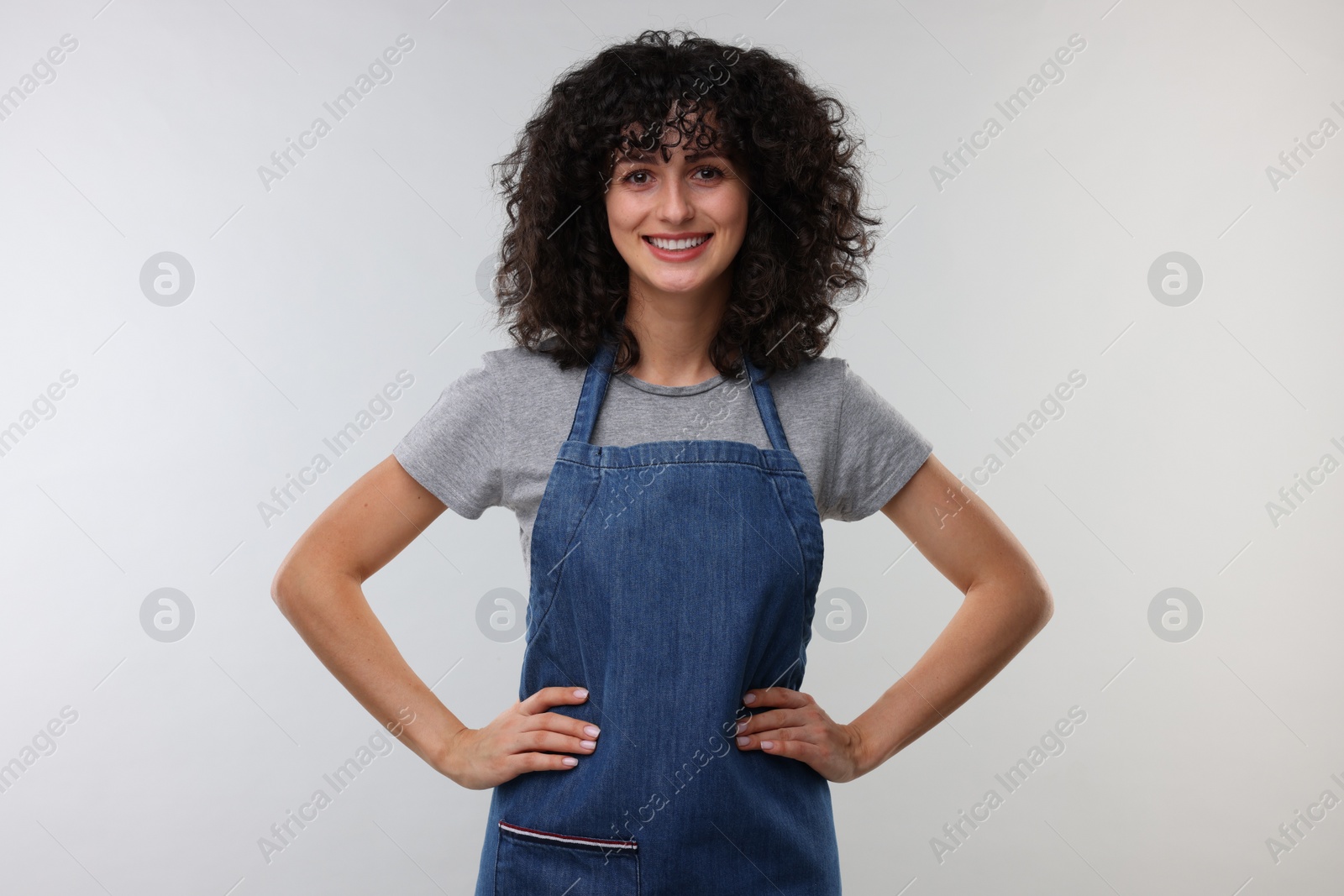 Photo of Happy woman wearing kitchen apron on light grey background. Mockup for design