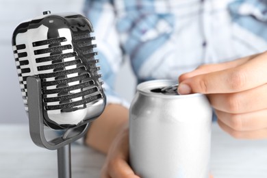 Photo of Woman making ASMR sounds with microphone and can at white table, closeup