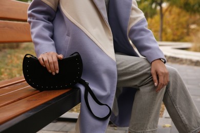 Photo of Stylish woman with trendy black baguette bag on bench in park, closeup