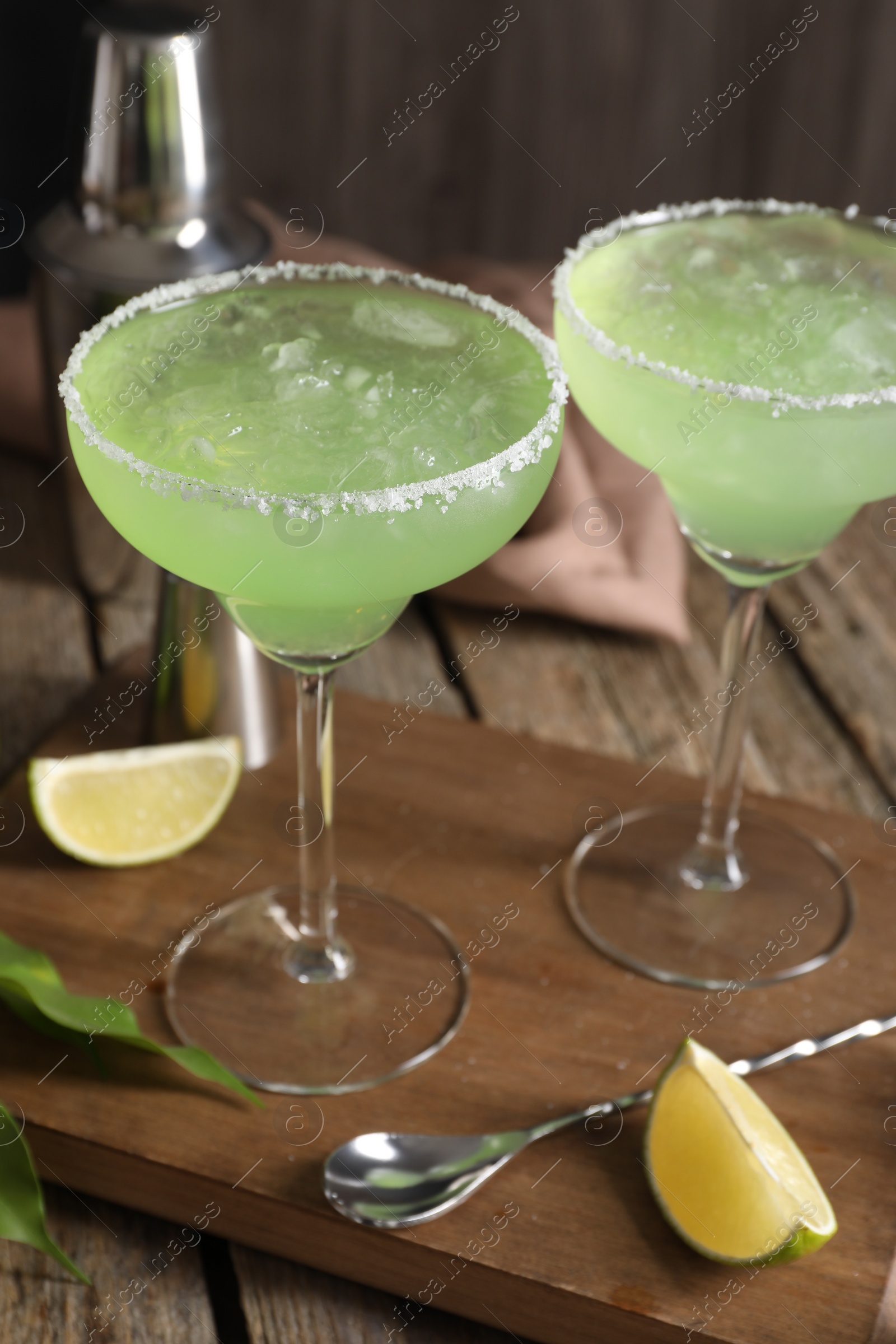 Photo of Delicious Margarita cocktail in glasses, lime and bar spoon on wooden table