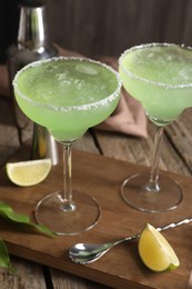 Photo of Delicious Margarita cocktail in glasses, lime and bar spoon on wooden table