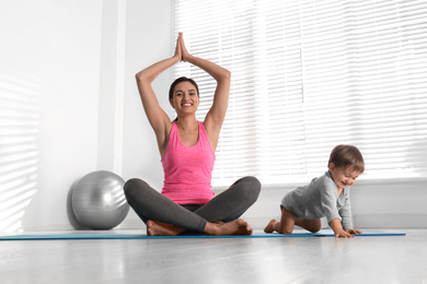 Photo of Young woman doing exercise with her son indoors. Home fitness