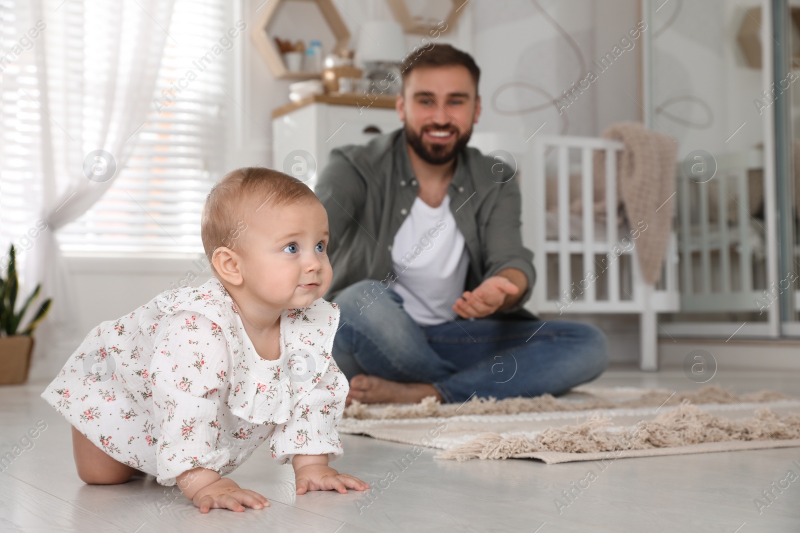 Photo of Happy young father watching his cute baby crawl on floor at home