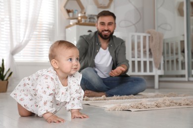 Photo of Happy young father watching his cute baby crawl on floor at home