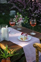 Vase with spring flowers, wine and cake on table served for romantic date in garden