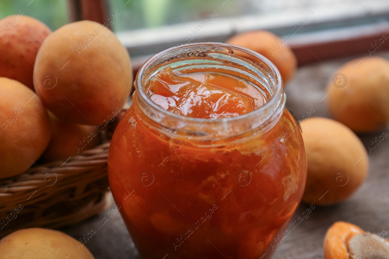 Photo of Jar of delicious jam and fresh ripe apricots on wooden table indoors, closeup. Fruit preserve