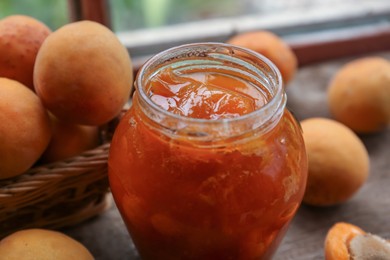 Photo of Jar of delicious jam and fresh ripe apricots on wooden table indoors, closeup. Fruit preserve