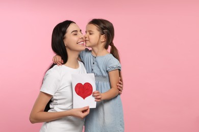 Happy woman with her cute daughter and handmade greeting card on pink background. Mother's day celebration