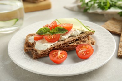 Photo of Fresh rye crispbreads with cream cheese and vegetables on light grey table, closeup