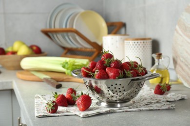 Metal colander with fresh strawberries on grey countertop in kitchen