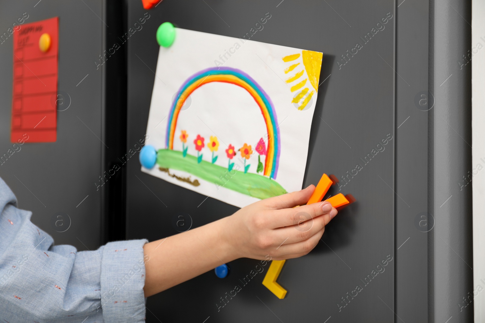 Photo of Woman putting child's drawing on refrigerator door, closeup