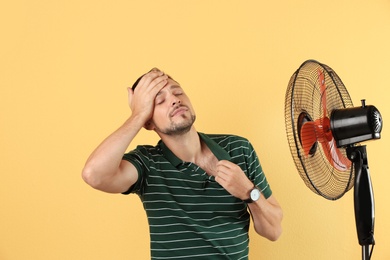 Man suffering from heat in front of fan on color background