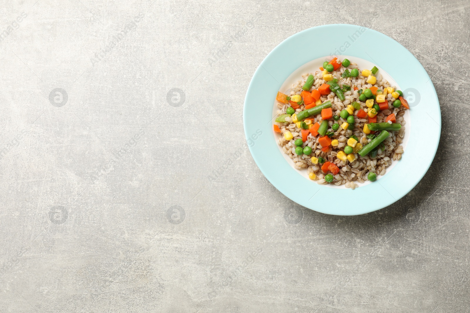 Photo of Tasty pearl barley porridge with vegetables on light textured table, top view. Space for text