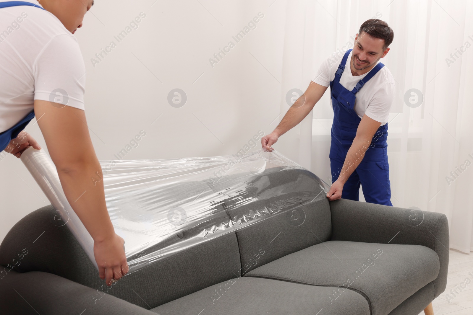 Photo of Workers wrapping sofa in stretch film indoors