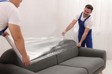 Workers wrapping sofa in stretch film indoors