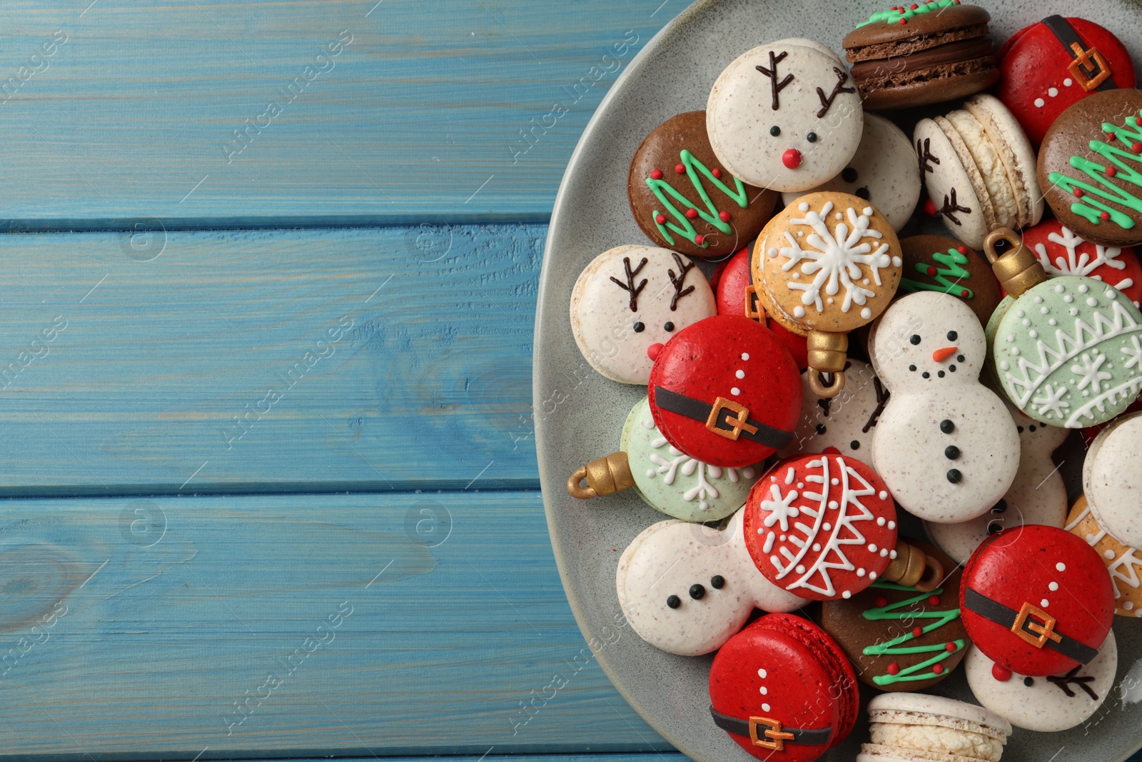 Photo of Beautifully decorated Christmas macarons on light blue wooden table, top view. Space for text