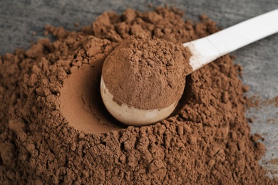 Pile of chocolate protein powder and scoop on grey table, closeup