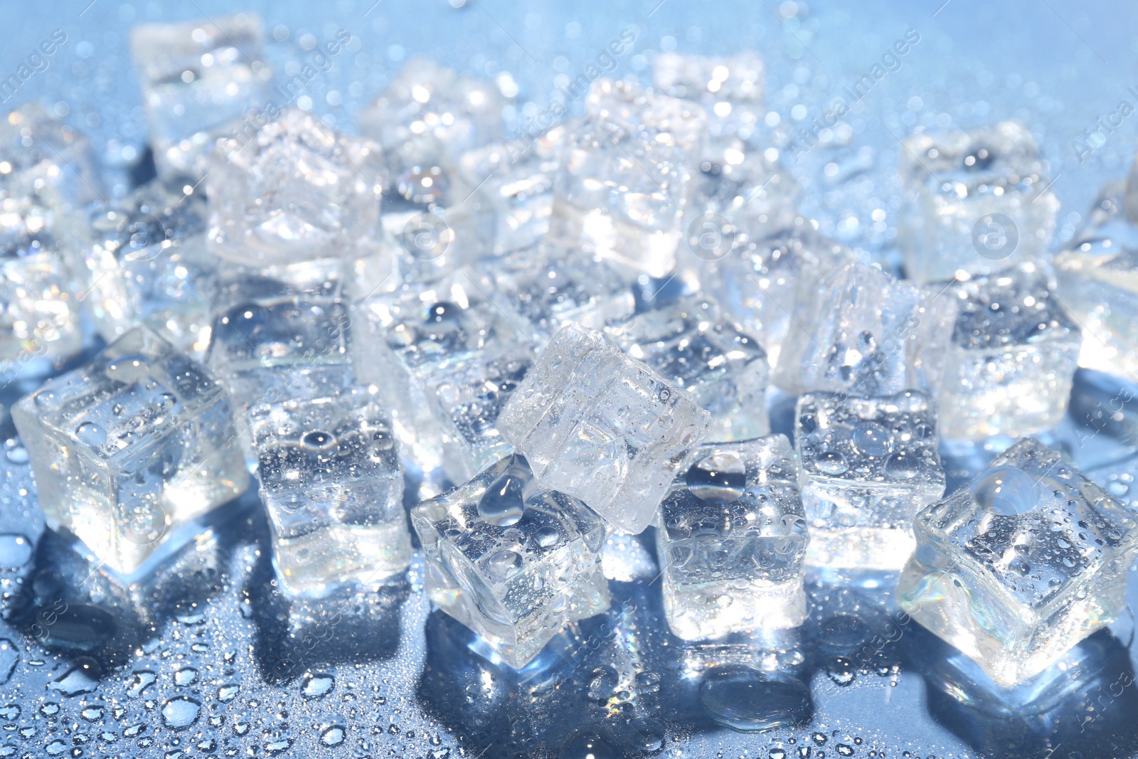 Photo of Melting ice cubes and water drops on blue background, closeup