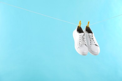 Stylish sneakers drying on washing line against light blue background, space for text