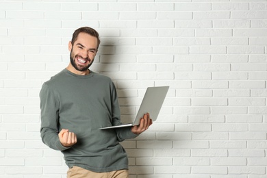 Photo of Emotional young man with laptop celebrating victory near brick wall. Space for text